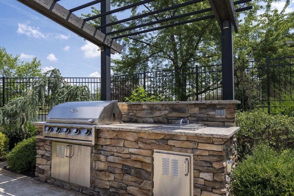 A stone outdoor kitchen with a grill and a pergola.