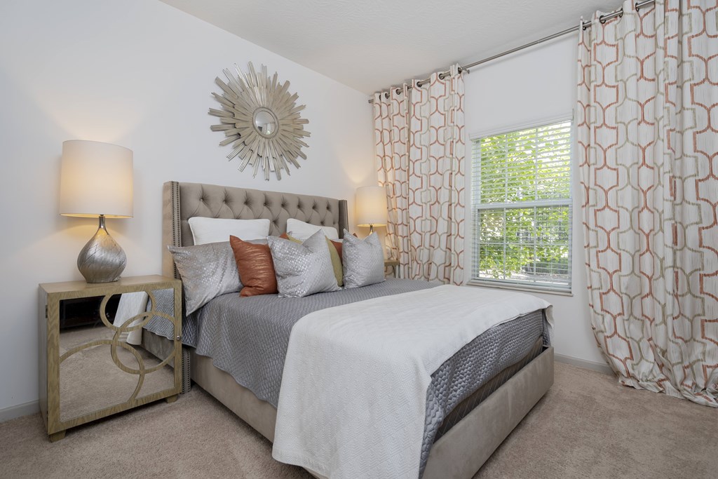 A bedroom with a large bed and a decorative sunburst mirror on the wall.