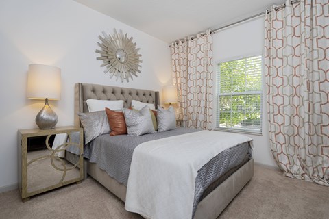 A bedroom with a large bed and a decorative sunburst mirror on the wall.