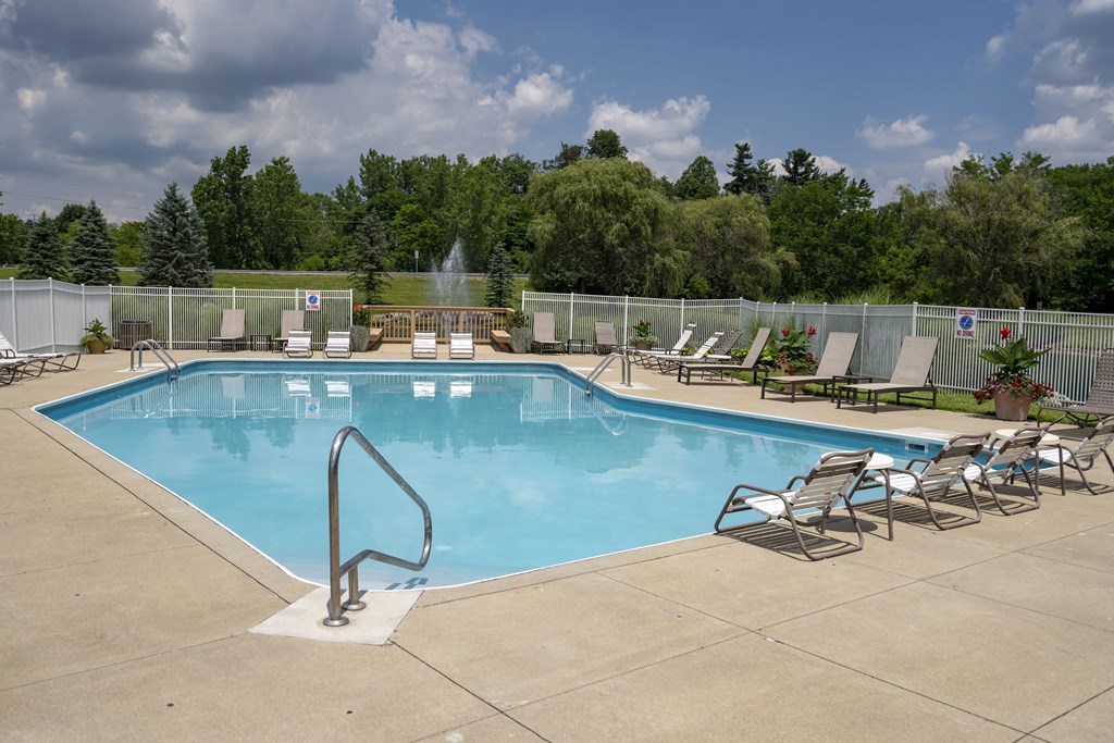 A large outdoor swimming pool surrounded by a fence and lounge chairs.