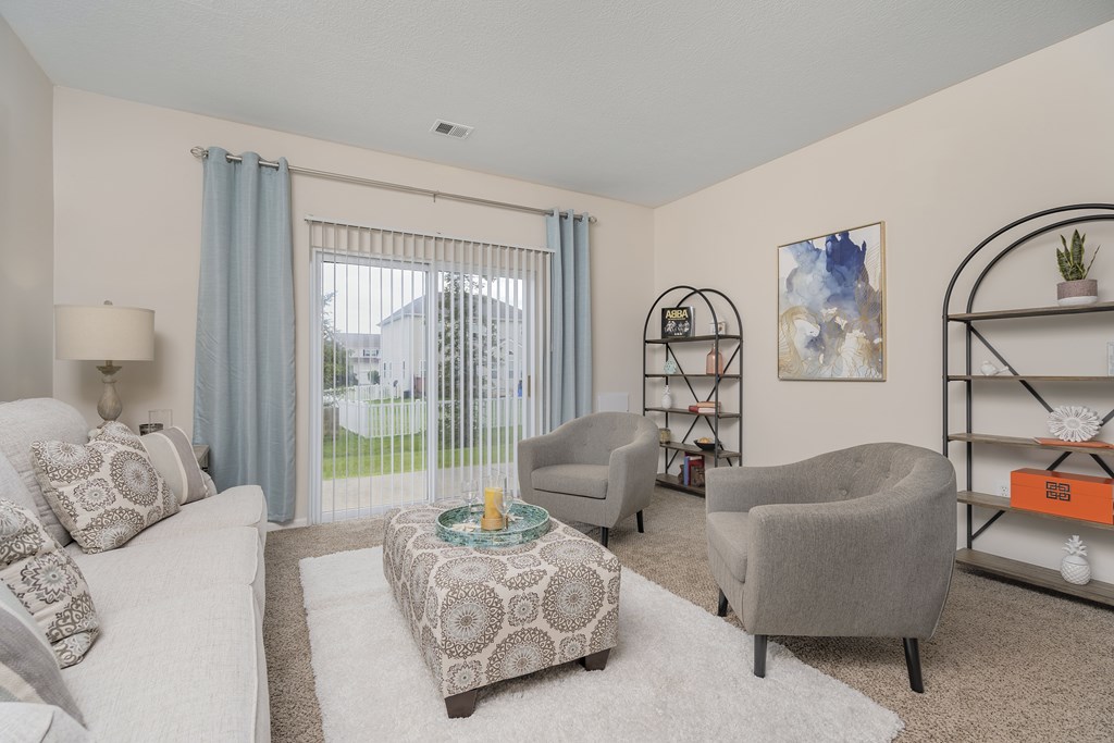 A living room with a white couch, grey armchair, and a patterned ottoman.