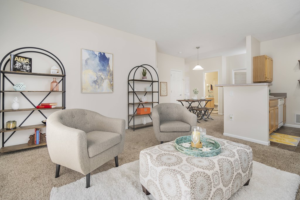 A living room with a beige armchair, a round ottoman, and a bookshelf.