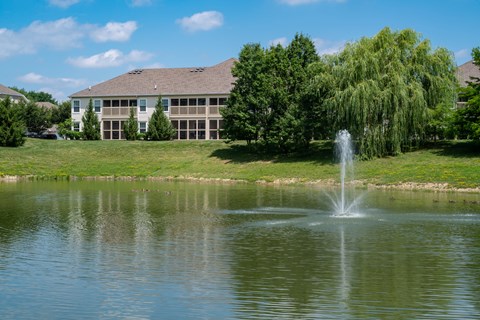 A fountain in the middle of a pond in front of a building.