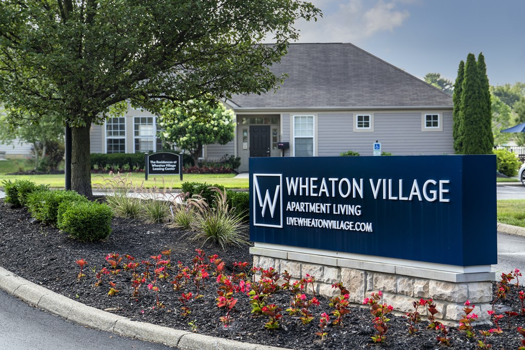 A blue sign that says Wheaton Village in front of a house.