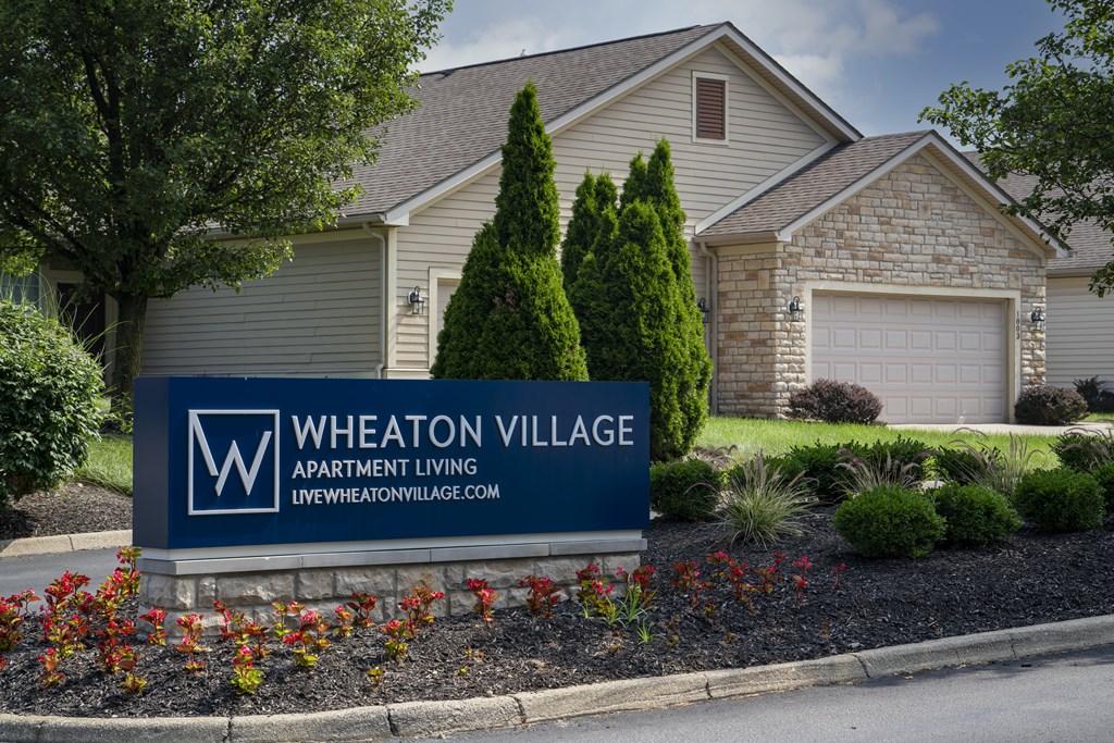 A sign for Wheaton Village Apartment Living in front of a house.