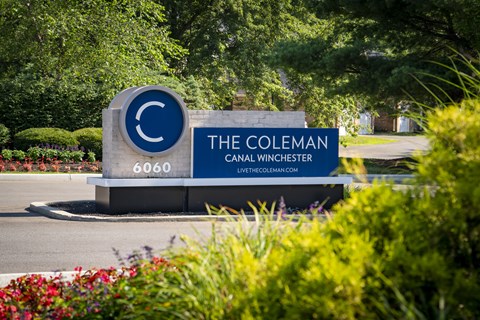 A sign for The Coleman Careal Winchester is displayed in front of some bushes.