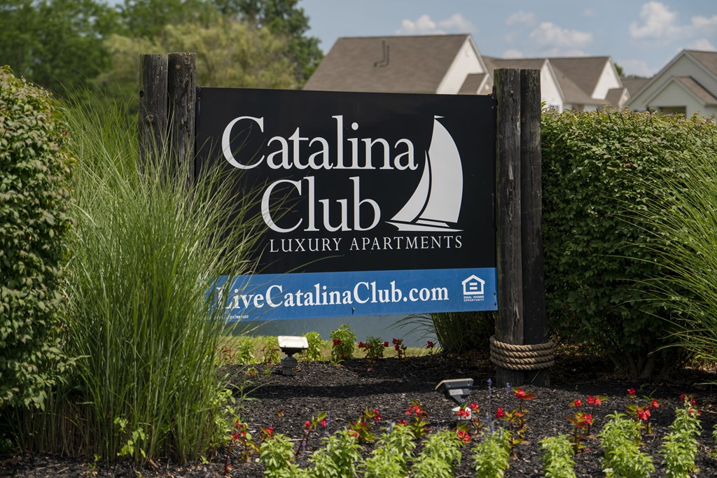 A sign for the Catalina Club Luxury Apartments is displayed in front of some greenery.