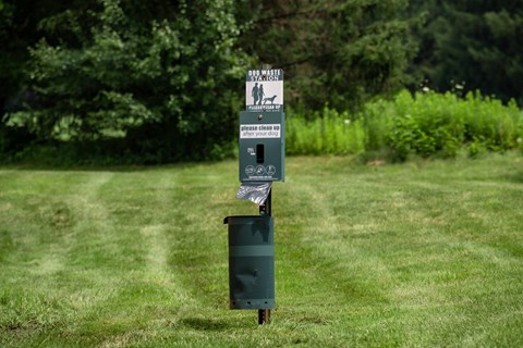 A trash can with a sign on it is in the grass.