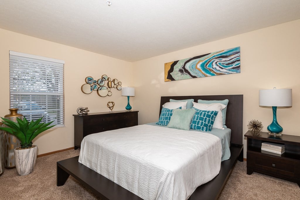 Two-bedroom apartment in Hilliard, OH featuring a cozy bedroom with carpet, bed, dresser, nightstands, and lamps