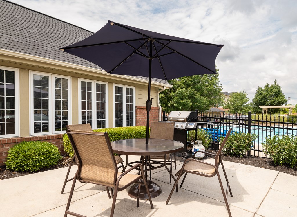 Apartments for Rent in Hilliard, OH - Residences at Breckenridge - BBQ Area Near the Pool with a Grill, a Table, Chairs, and an Umbrella