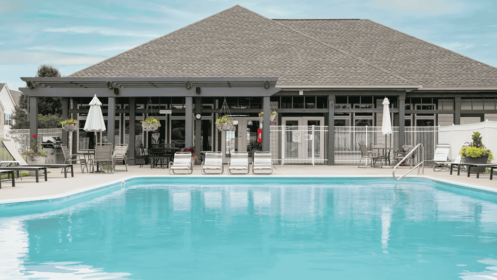 A large swimming pool in front of a building with a covered patio.