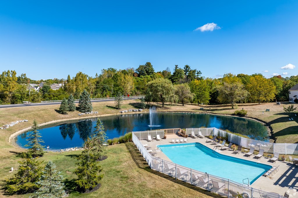 A large outdoor swimming pool surrounded by a fence and a smaller pond.