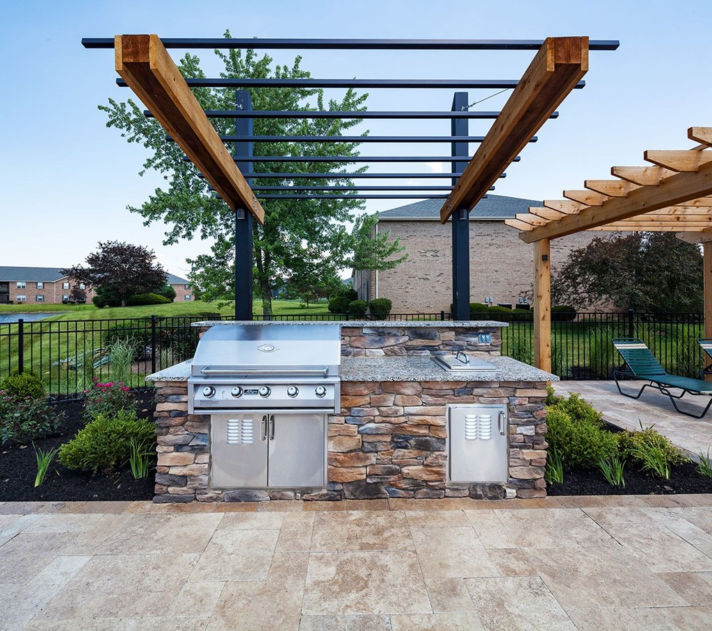 A BBQ grill is built into a stone structure with a wooden pergola above it.