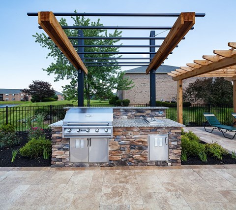 A BBQ grill is built into a stone structure with a wooden pergola above it.
