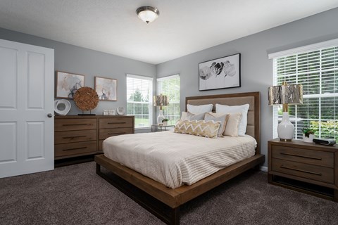 Large carpeted bedroom at Carson Farms with a bed, nightstands, dresser, lamps, and three bright windows