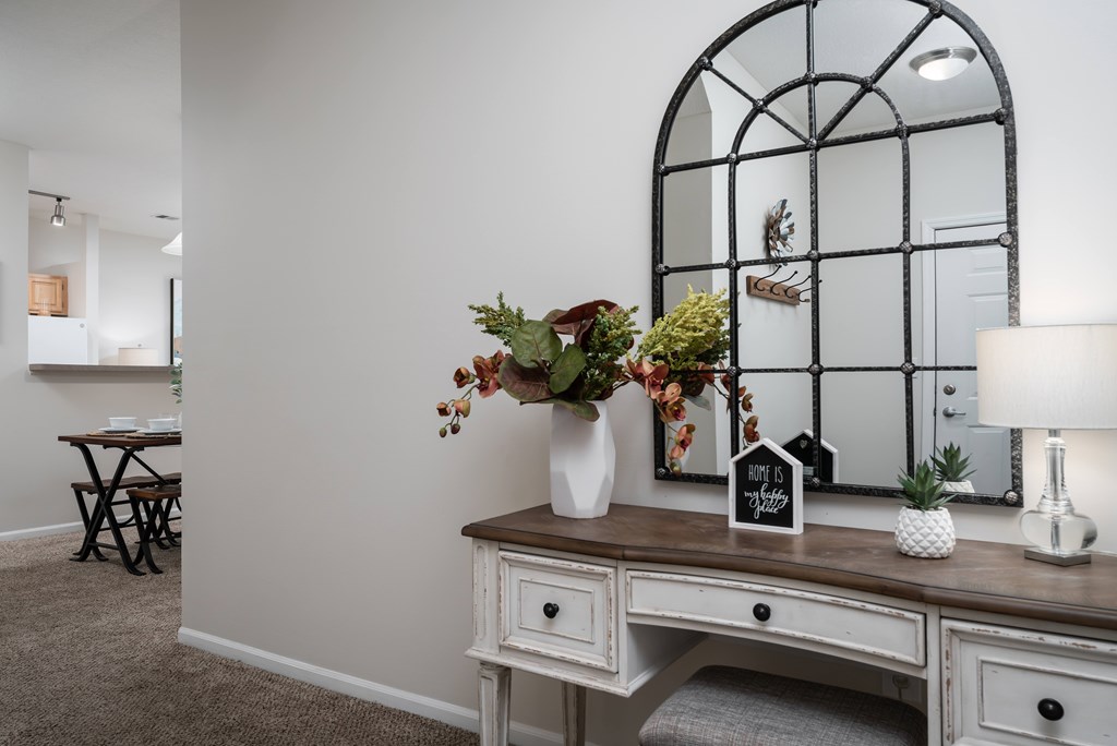 A white desk with a mirror and a vase of flowers.