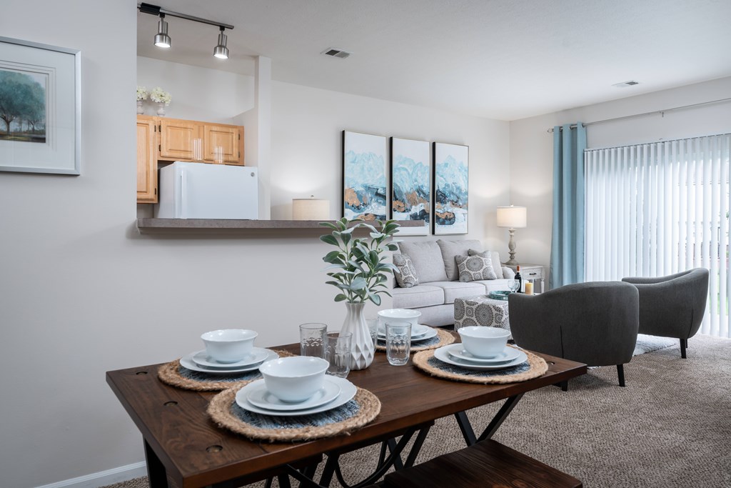 A dining table set with plates and glasses is in the foreground of a well-lit dining room.