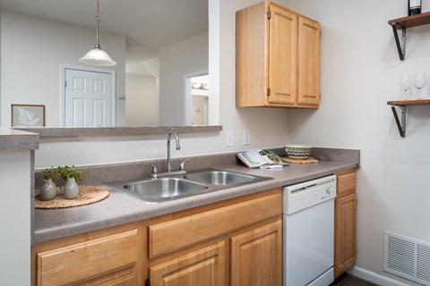 Kitchen at Catalina Club in Pataskala, OH, featuring wood-style cabinetry, grey countertops, a breakfast bar, and a white dishwasher.