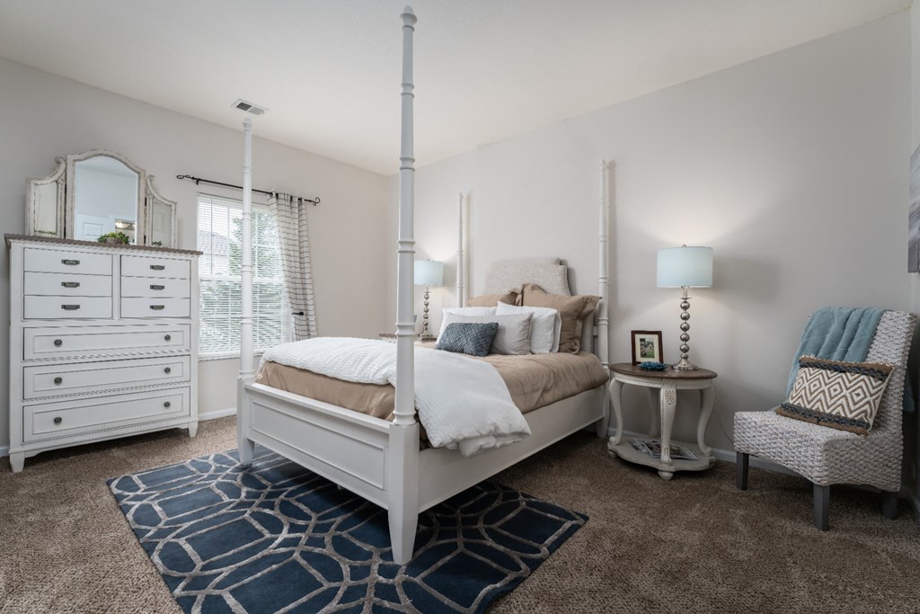 Pet-Friendly Apartments in Pataskala, OH - Catalina Club - Bedroom with Chair, Bed, Dresser, Nightstands, Lamps, Area Rug, and Window.