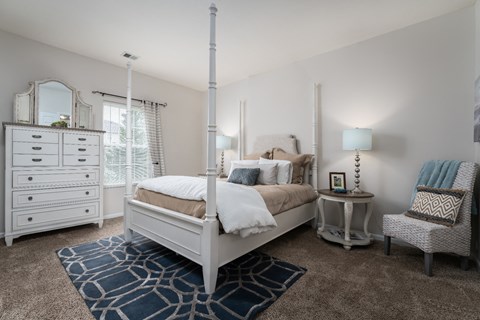 Pet-friendly bedroom at Catalina Club Apartments in Pataskala, OH, with a cozy bed setup, dresser, chair, nightstands, and natural light from the window.