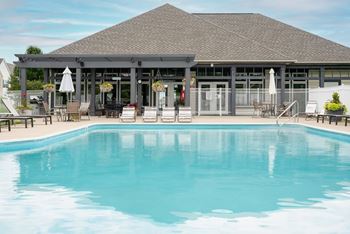 A large swimming pool in front of a building with a covered patio.