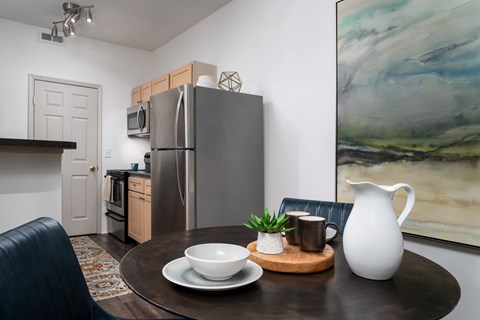 A modern kitchen with a refrigerator, a dining table with a bowl, a plant, and a jug.
