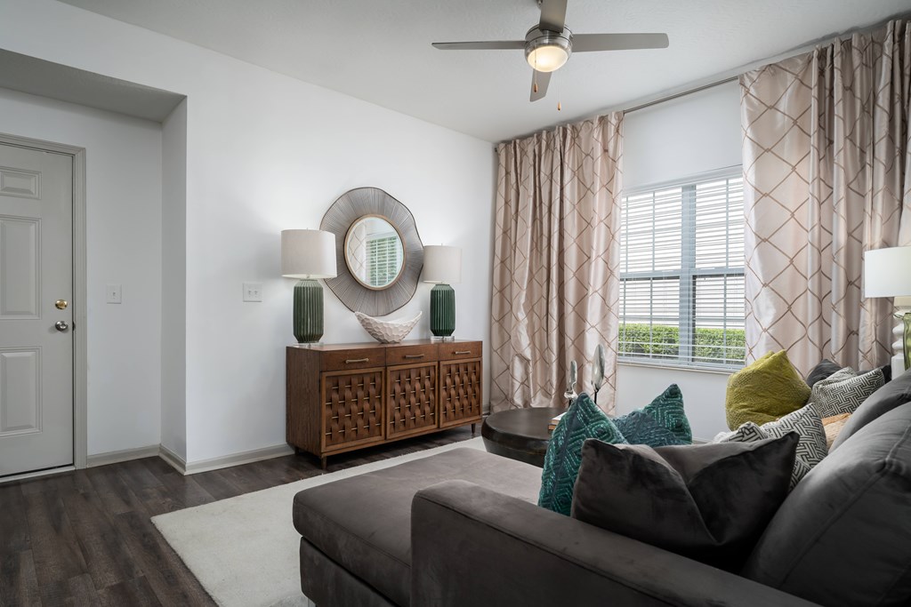 A living room with a grey couch, a wooden side table, and a ceiling fan.
