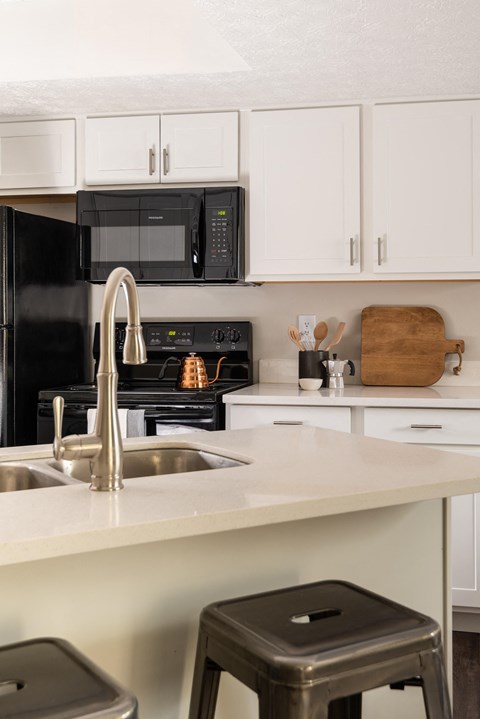 A kitchen equipped with black appliances, sleek white cabinets, and two barstools.
