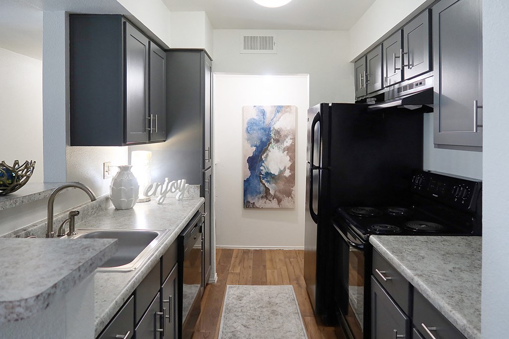 Modern kitchen with black appliances, granite countertops, sleek cabinetry, and wood-style flooring in a two-bedroom apartment at The Boulevard in Florence, KY