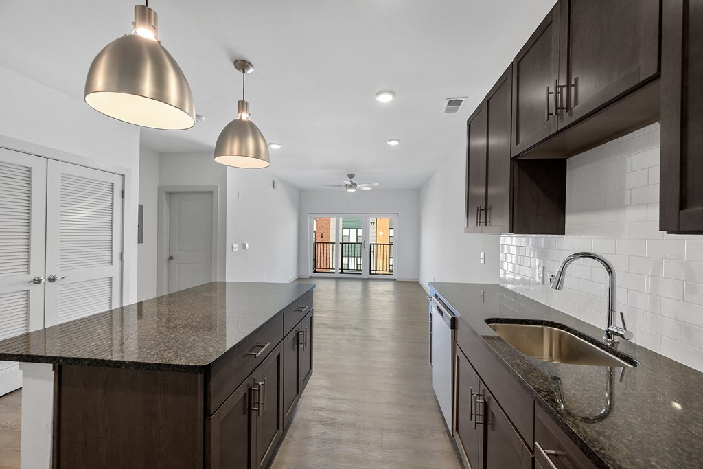 Madamore kitchen with dark wood cabinets and an island, next to a living room with a sliding glass door.
