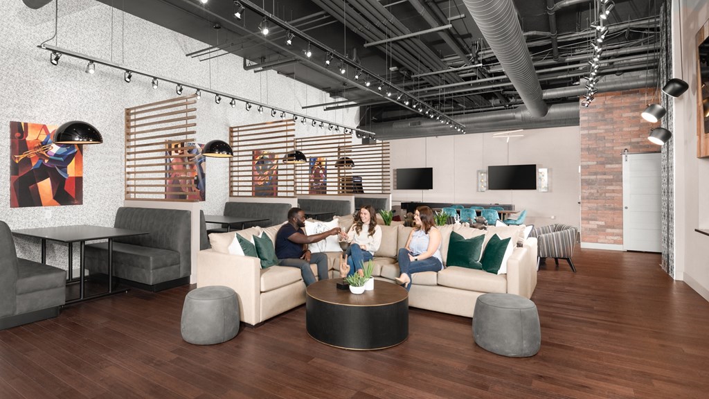 Three people sitting on a beige couch next to booth tables on hardwood-style flooring.