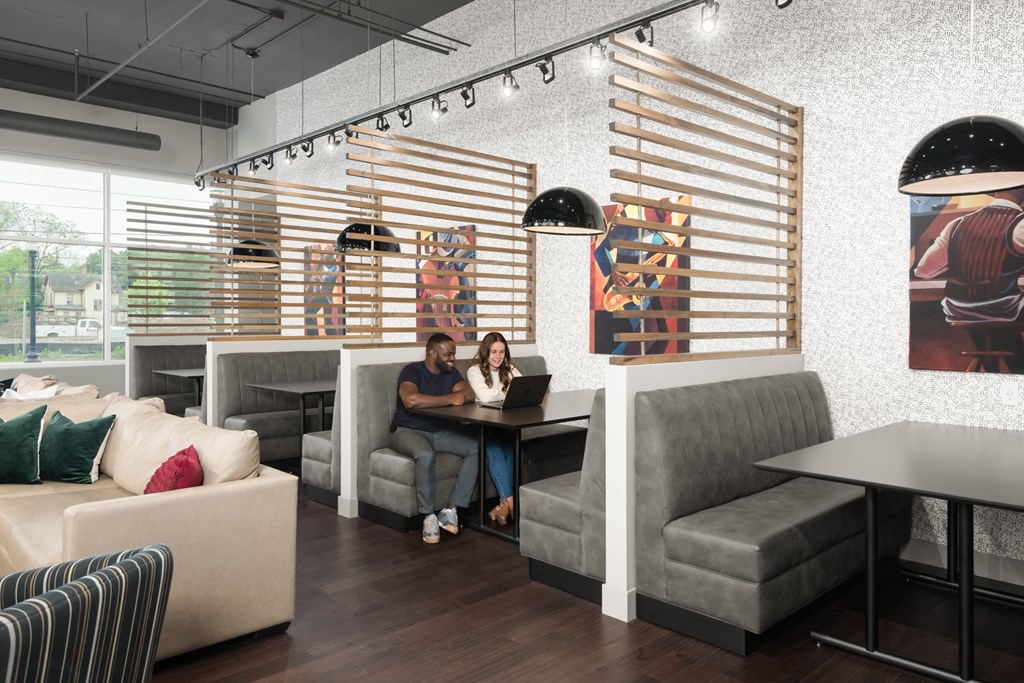 Co-working lounge with booth tables next to a beige couch, and light fixtures,
