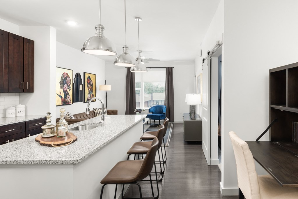 A kitchen with a spacious island with three barstools, next to a living room at Madamore Apartments.