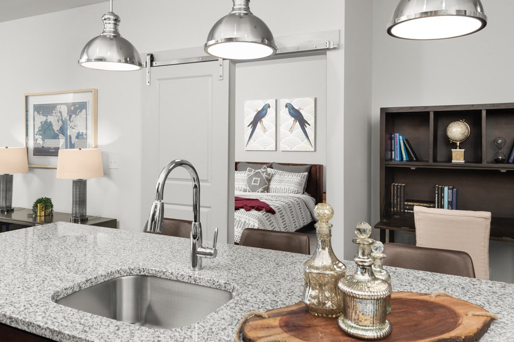 A kitchen island with a sink and granite countertops, and light fixtures.