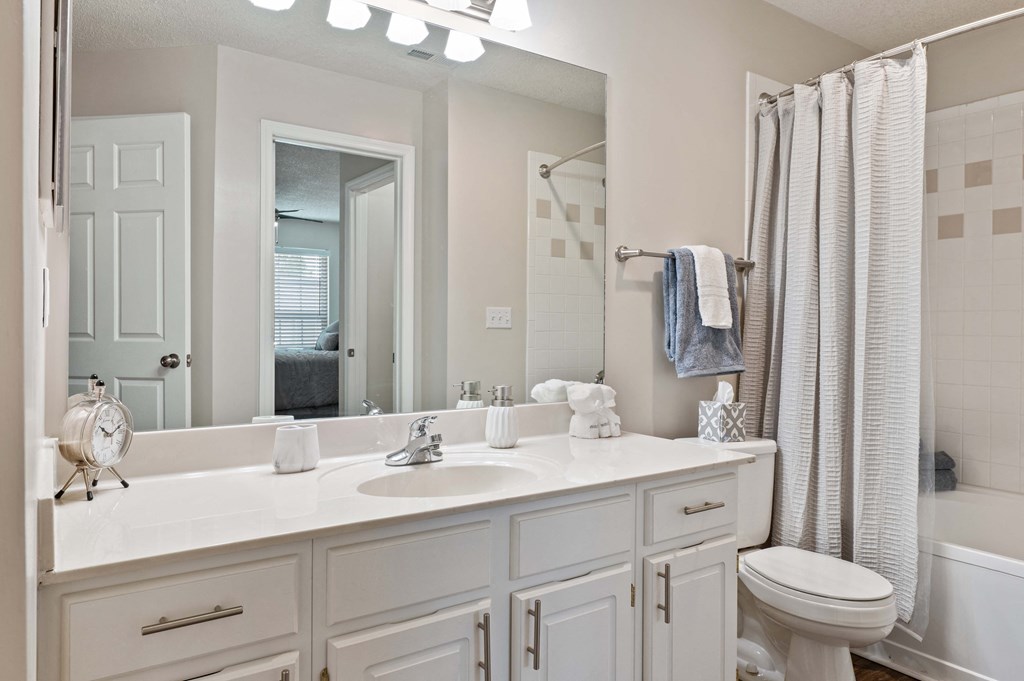 Two-Bedroom Apartments in Hamburg, KY - Reserve at Hamburg - Bathroom with a Large Vanity Mirror, White Cabinets, Wood-Style Flooring, and a Shower with a Bathtub