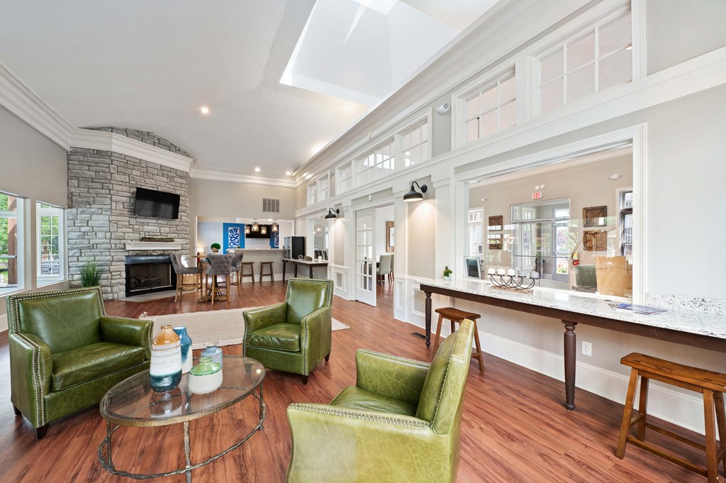 Resident clubhouse with a table surrounded by three green chairs, next to a selection of seating areas and a fireplace.