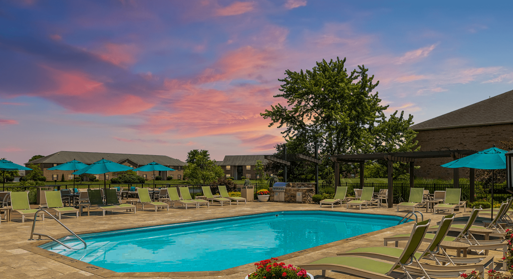 Resort-style swimming pool with lounge chairs and umbrellas, located beside a charming brick building at The Coleman in Canal Winchester, OH