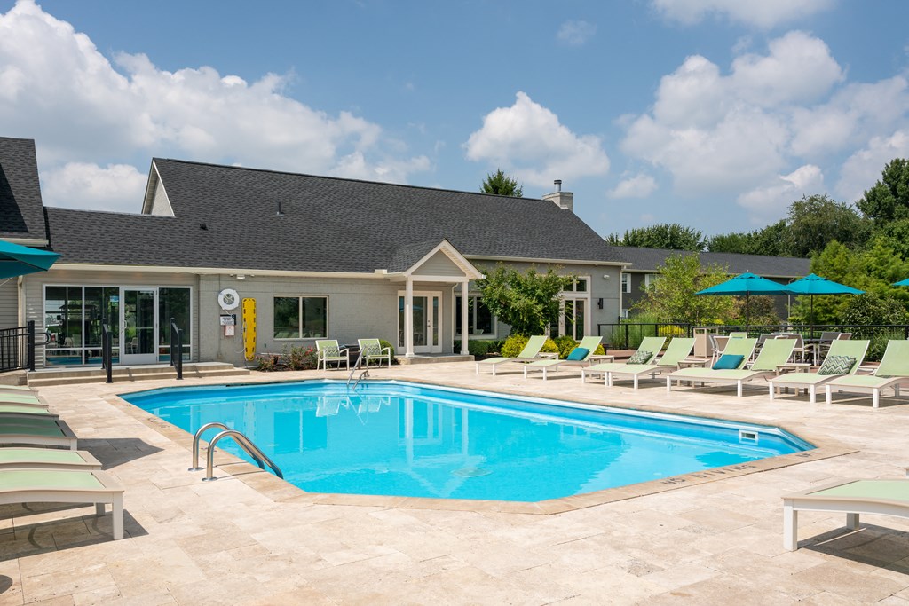 a swimming pool with chaise lounge chairs and sun umbrellas in front of a gray