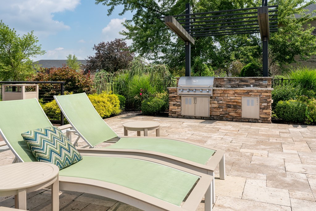 a patio with a grill and two lounge chairs