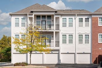 A white two story apartment building with a tree in front.