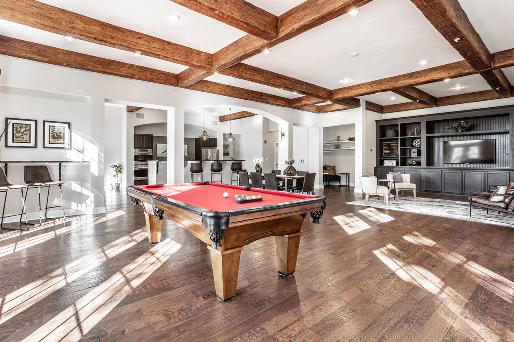 A pool table is in the middle of a room with wooden floors and a high ceiling.