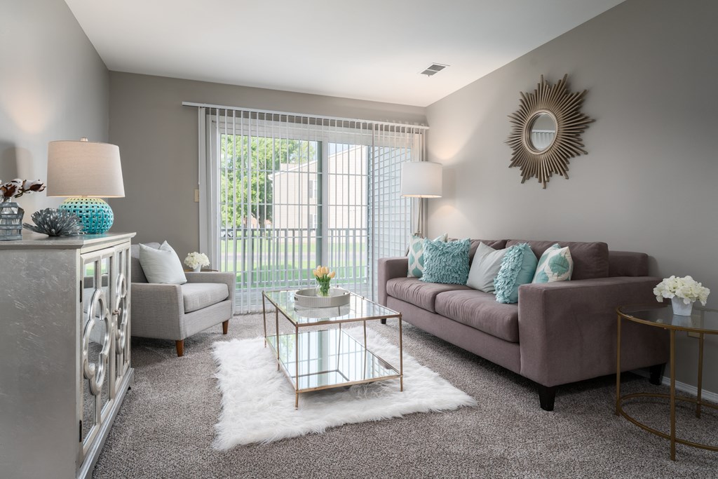 3 BR Apartments in Reynoldsburg, OH - The Oaks - Carpeted Living Room with Couch, Chair, Coffee Table, Cabinet, Floor Lamp, and Sliding Glass Door Leading to Patio