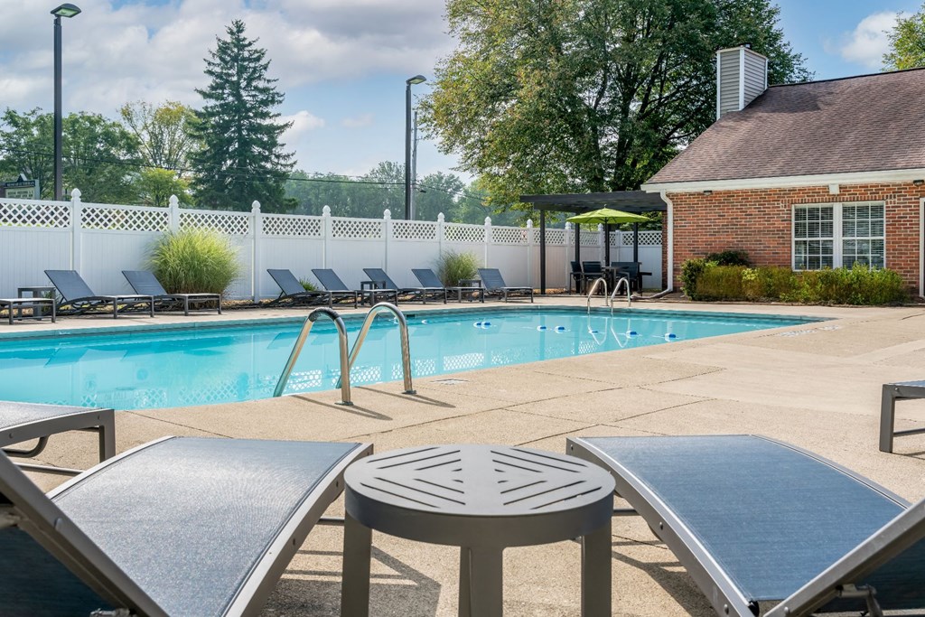 a swimming pool with lounge chairs and tables in front of a brick building with a white fence