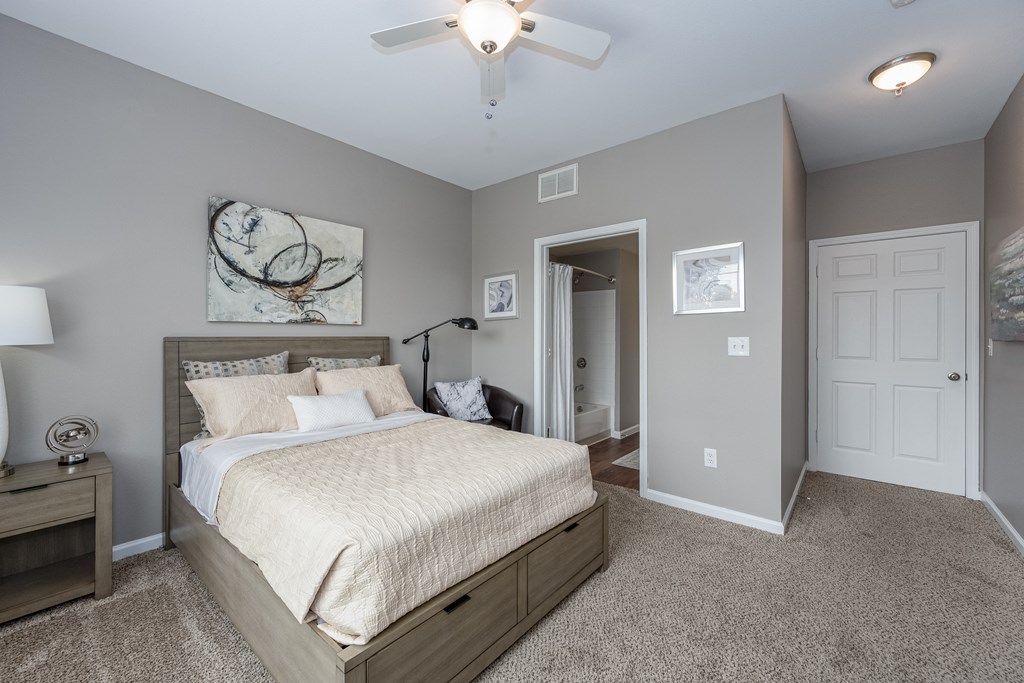 Florence, KY Apartments - Trellises - Bedroom with Bed, Chair, Nightstand, Lamp, Floor Lamp, Ceiling Fan, and Attached Bathroom.