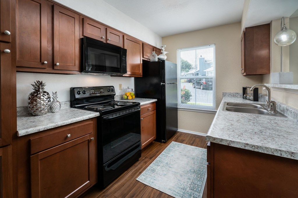 One BR Apartments in Florence KY - Windridge Townhomes - Kitchen with Marble-Style Countertops, Brown Cabinets, Window, and Black Appliances