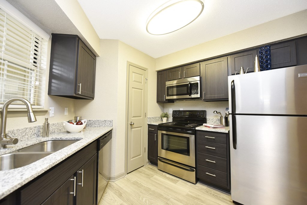 2-Bedroom Apartments in Fishers, IN - Metropolitan Fishers - Modern Kitchen with Stainless Steel Appliances, Dark Wood Cabinetry, Granite Countertops, Wood-Style Flooring, and a Window