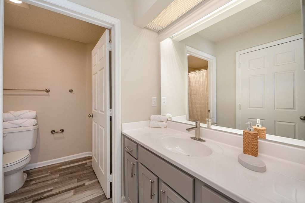 A bathroom equipped with white furniture, a mirror, and hardwood-style flooring.