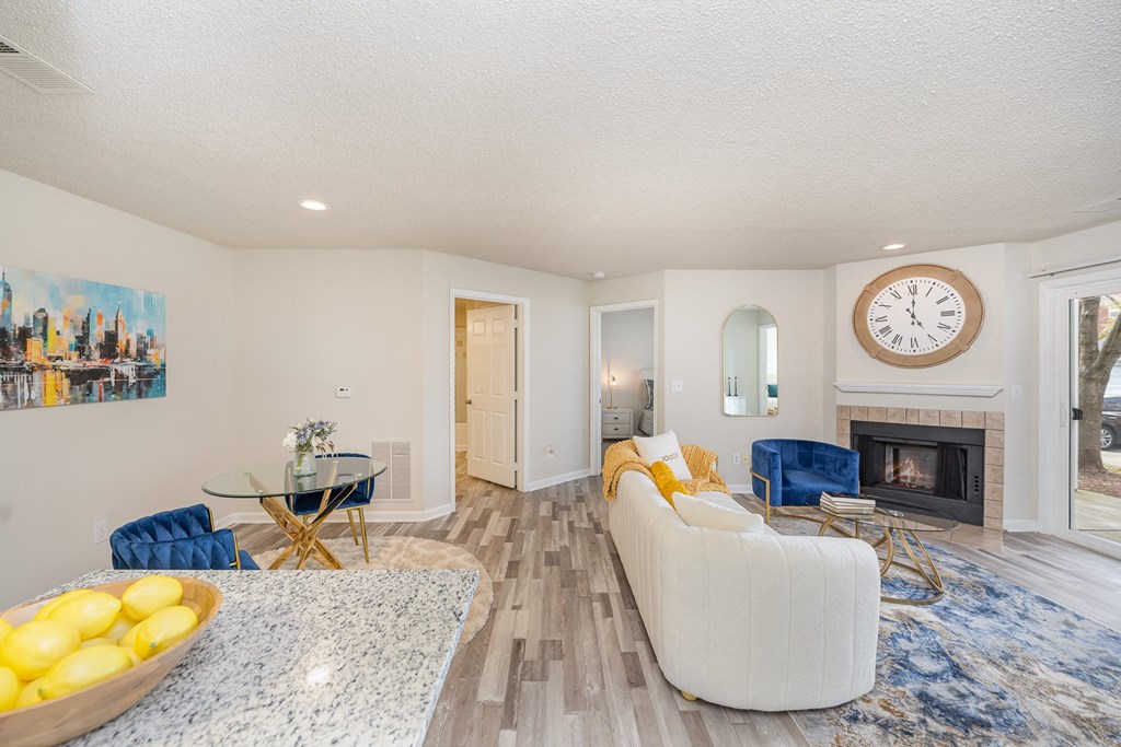 A dining room with a table surrounded by two chairs, next to a living room with a couch, chair, and fireplace.