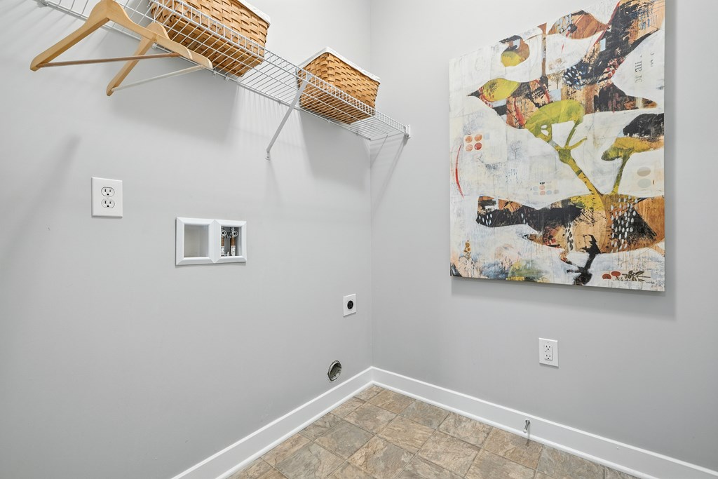 A room with a large painting on the wall and a wooden hanger with a basket on top of a clothes rack.