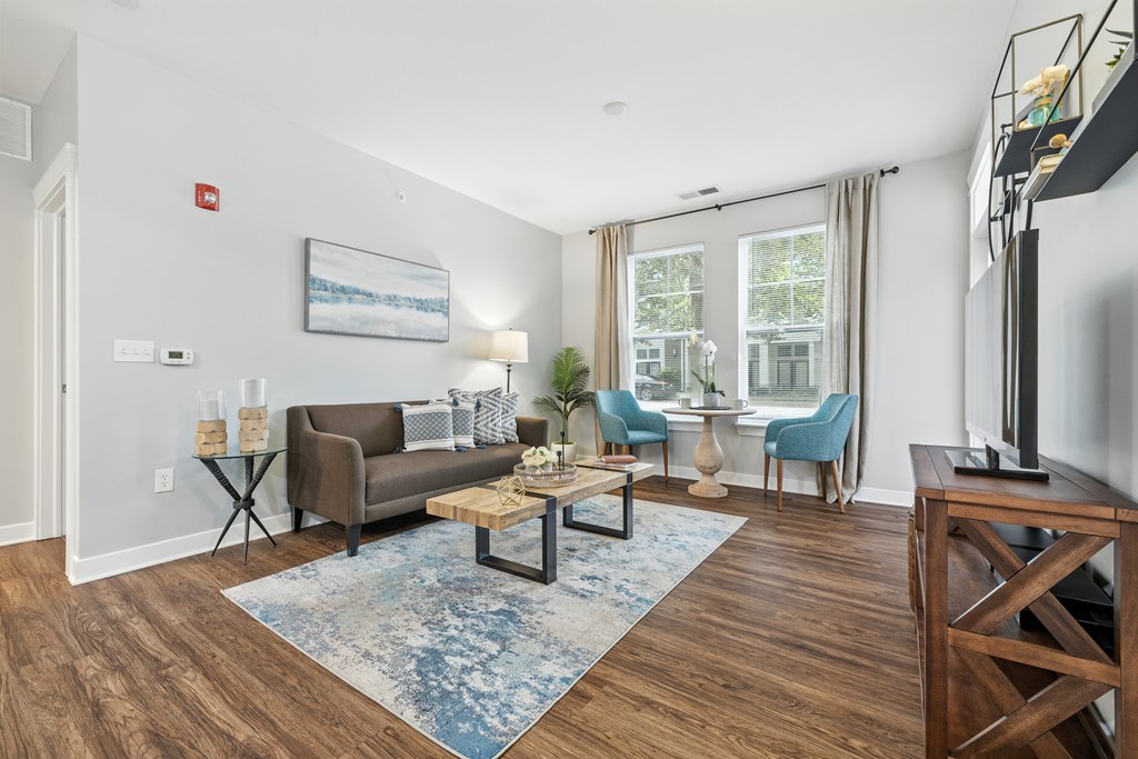 A living room with a brown couch, blue chairs, and a painting on the wall.